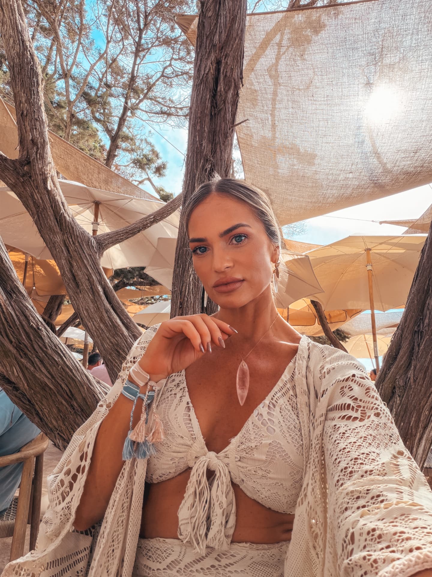 Emilim de renda branca num beach club, com o mar e os guarda-sóis ao fundo, em Ibiza