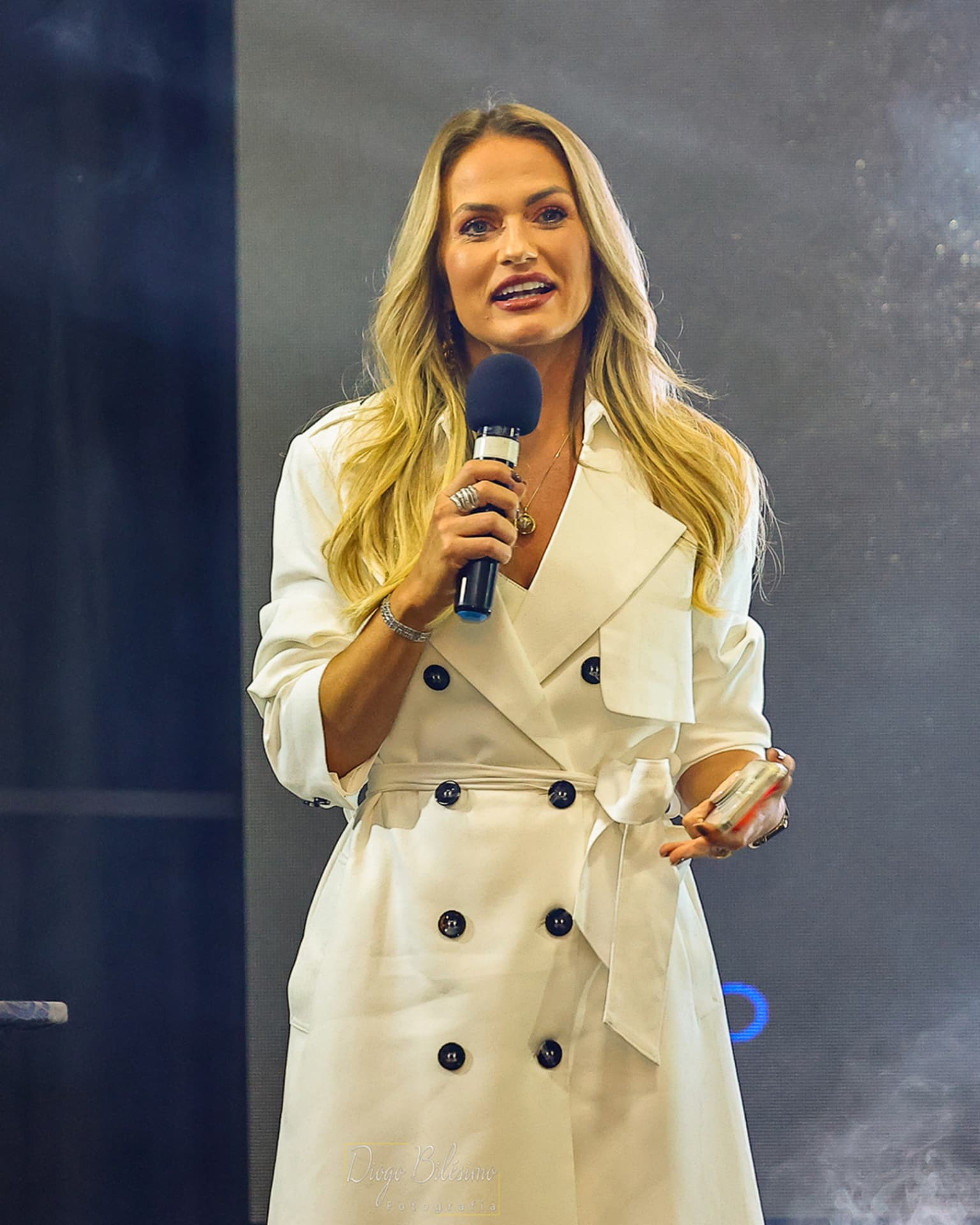 Emilim de branco no palco, falando ao microfone durante uma palestra