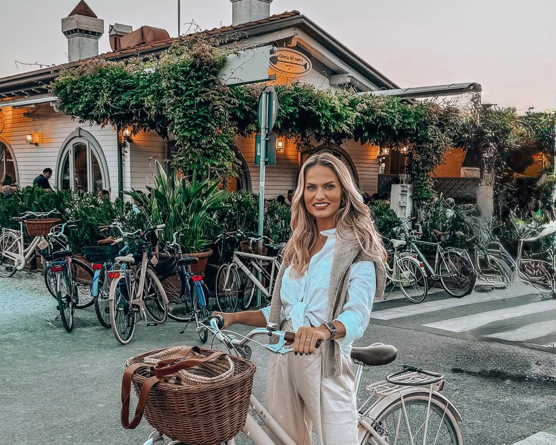 Emilim com uma bicicleta de cesta, parada diante de uma osteria à beira-mar