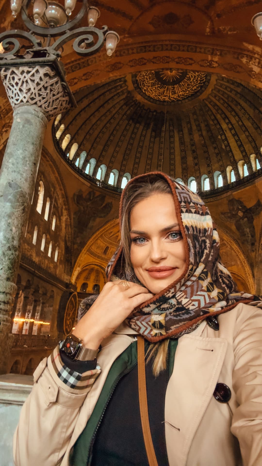 Emilim de casaco bege e lenço geométrico na Santa Sofia, em Istambul, com a coluna de mármore e as cúpulas decoradas ao fundo