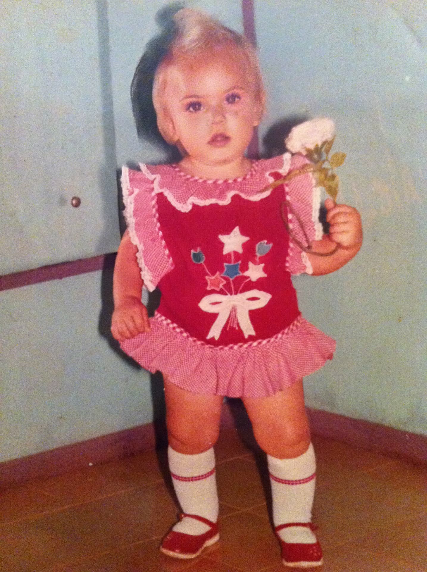 Emilim criança de vestido vermelho, com uma flor branca na mão