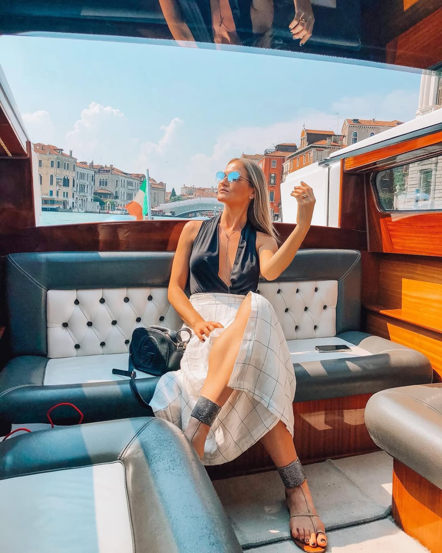Emilim sentada no banco de um táxi aquático em Veneza, com o canal ao fundo